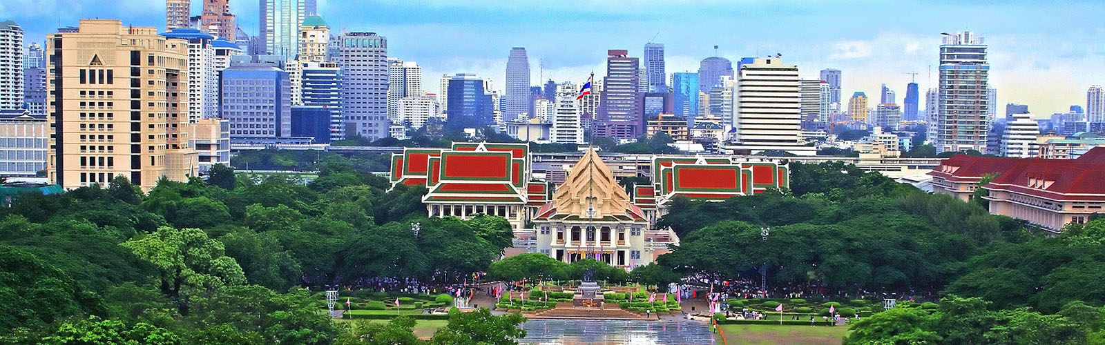 A large tree-covered park in the foreground and Bangkok's modern skyline in the background.